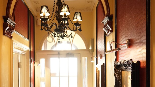 A hallway with a chandelier, a door, and a mirror on the wall. - Regency Hotel (Brighton)