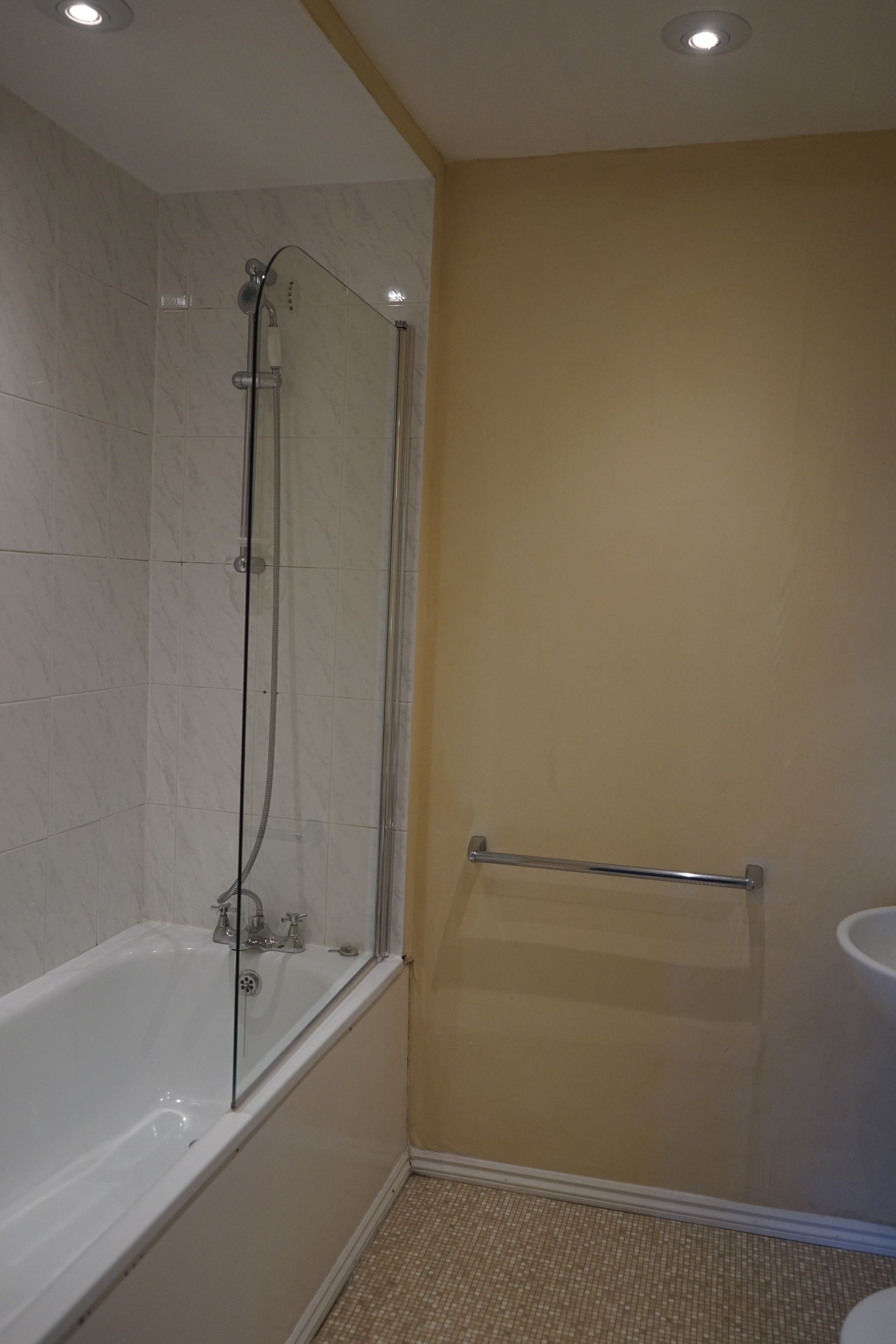 A bathroom with a glass-enclosed shower, a bathtub, and a handrail.