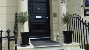 A black door with the number 28, flanked by two potted plants, leading to a staircase with a black railing. - Regency Hotel (Brighton)
