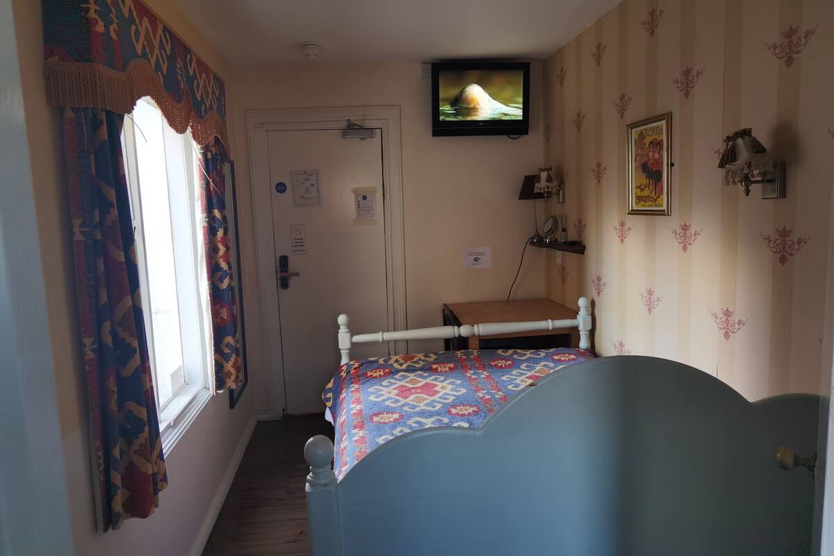 A bedroom with a bed, a television on the wall, a door, and patterned curtains.