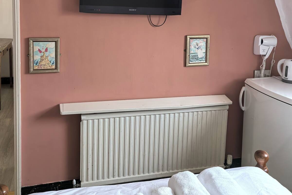 A hotel room with a television mounted on the wall, a radiator below, and a bed with rolled towels.