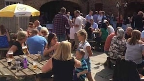 A courtyard with brick buildings, outdoor seating, and people gathered. - The New Inn (Beverley)