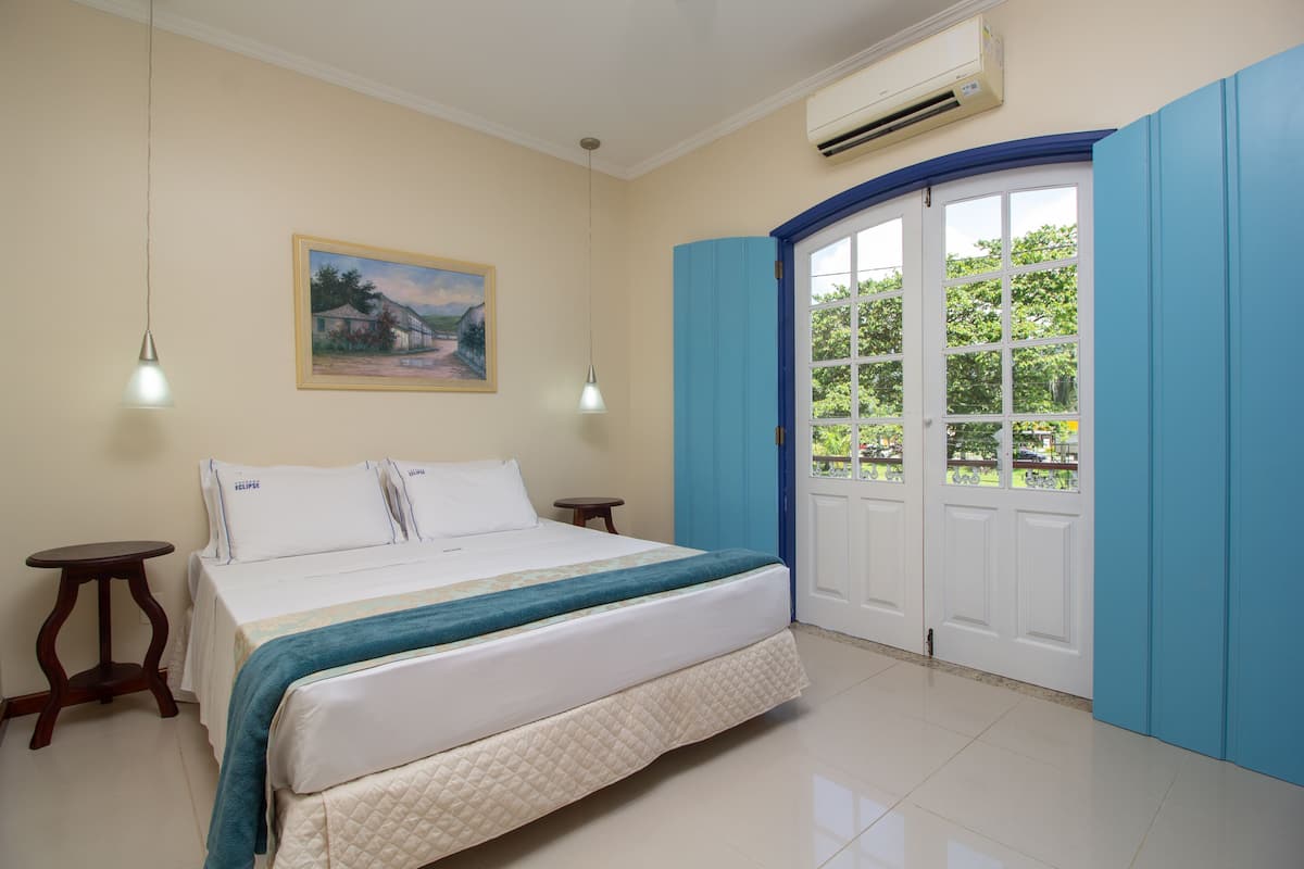 A bedroom with a bed, two bedside tables, a painting on the wall, and a door leading to a balcony.