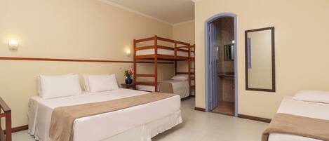 A hotel room with a bunk bed, a single bed, a bathroom with a mirror, and a small table with a vase.