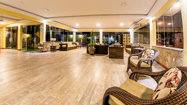 A spacious indoor area with wicker furniture, glass walls, and a wooden floor. - Pousada Eclipse (Paraty)