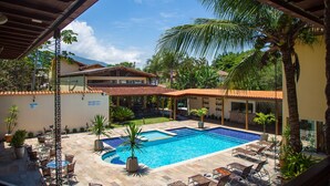 A pool area with lounge chairs, a covered seating area, and a building with a tiled roof. - Pousada Eclipse (Paraty)