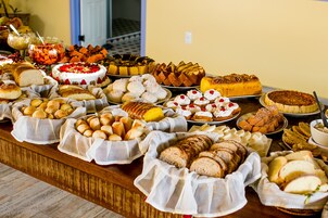 Uma mesa de buffet com diversos pães, doces e sobremesas.