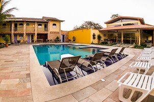 Piscina com espreguiçadeiras e um pátio com ladrilhos de pedra.