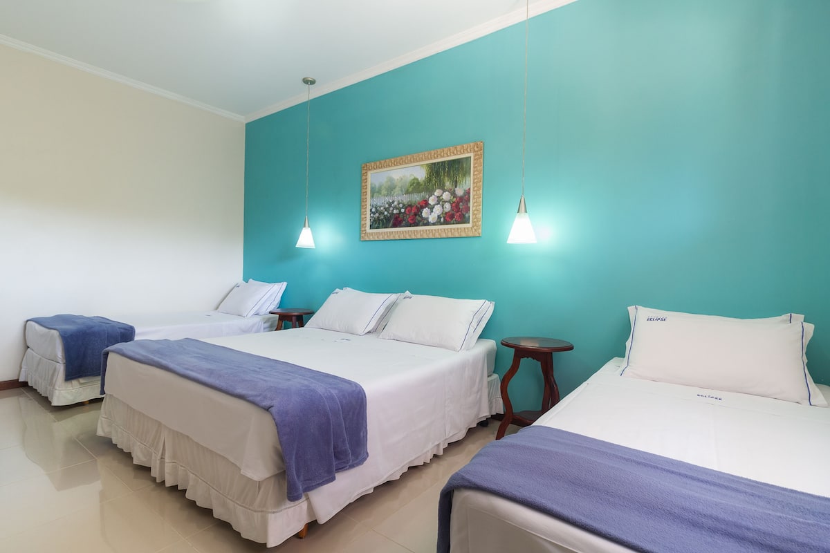 A hotel room with two beds, a teal accent wall, a framed picture, and pendant lights.