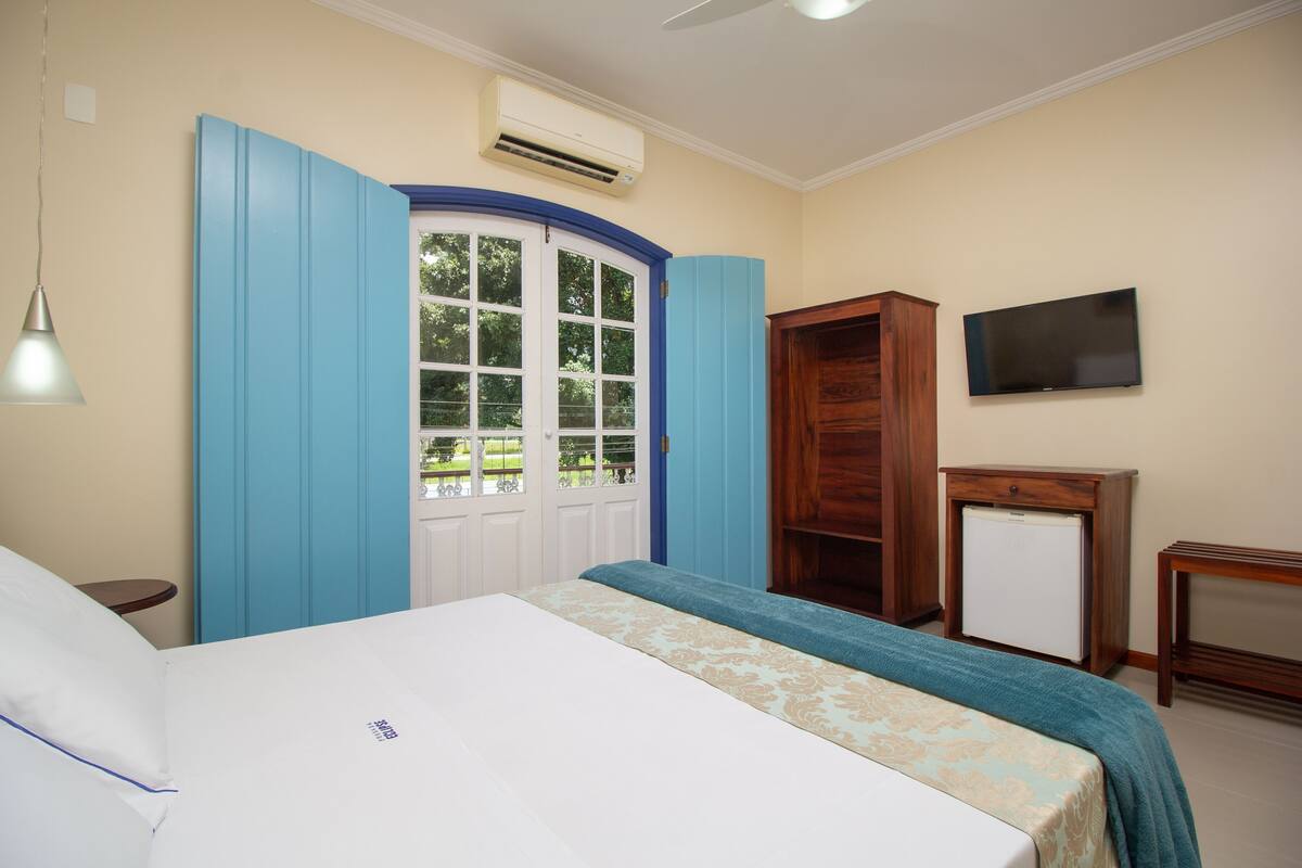 A bedroom with a bed, a wardrobe, a television, and a small refrigerator.