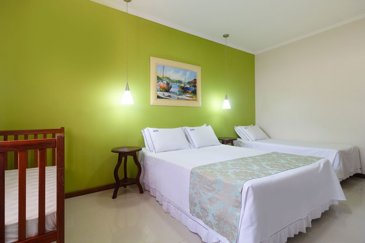 A room with two beds, a wooden crib, a small round table, and a painting on the wall.
