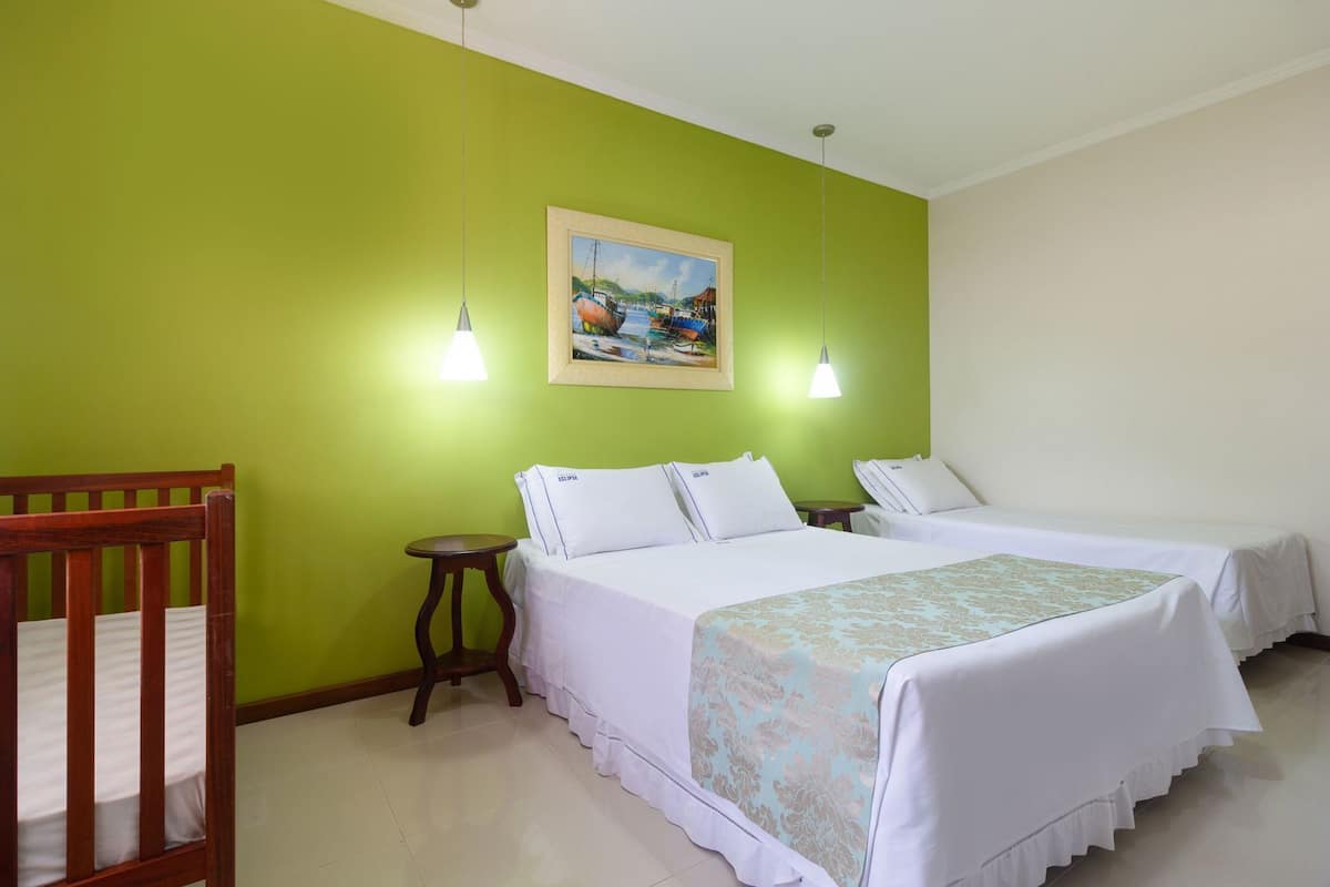 A room with two beds, a wooden crib, a small round table, and a painting on the wall.