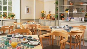 A dining area with wooden chairs and tables, a window with potted plants, and a shelf with books and decorative items. - Kocks Hotel (Hamburg)