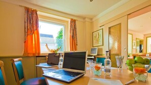 A hotel room with two laptops on a desk, a bottle of water, a bowl of apples, and a vase with a flower. - Kocks Hotel (Hamburg)