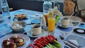 A breakfast table with various food items, a bottle of water, and a view of the sea through the window. - Eliros Studios (Chania)