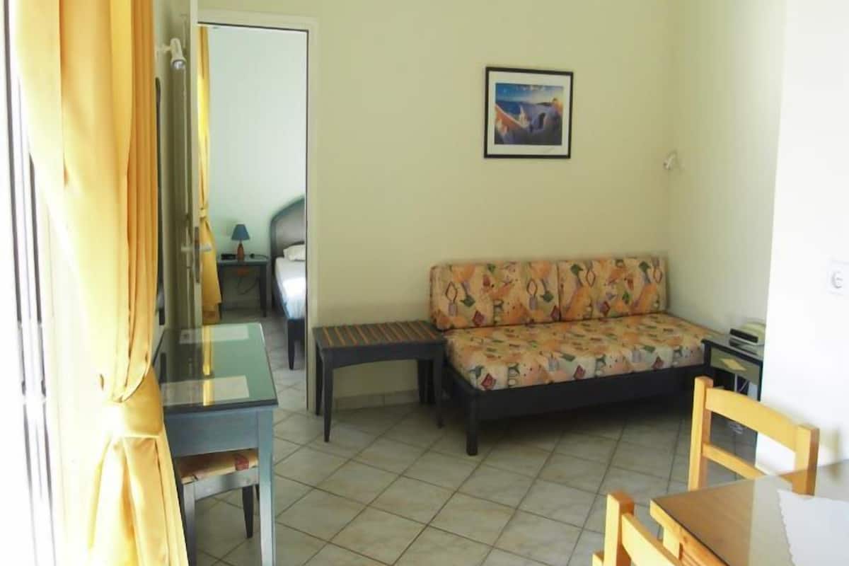 Una habitación con un sofá, una mesita, una silla, una cama y un cuadro en la pared.