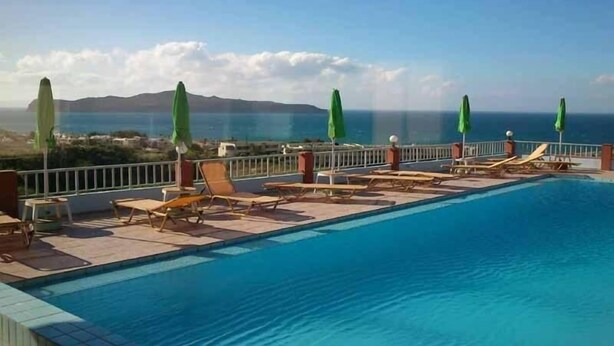 A pool with lounge chairs and umbrellas, overlooking a coastal view. - Eliros Studios (Chania)