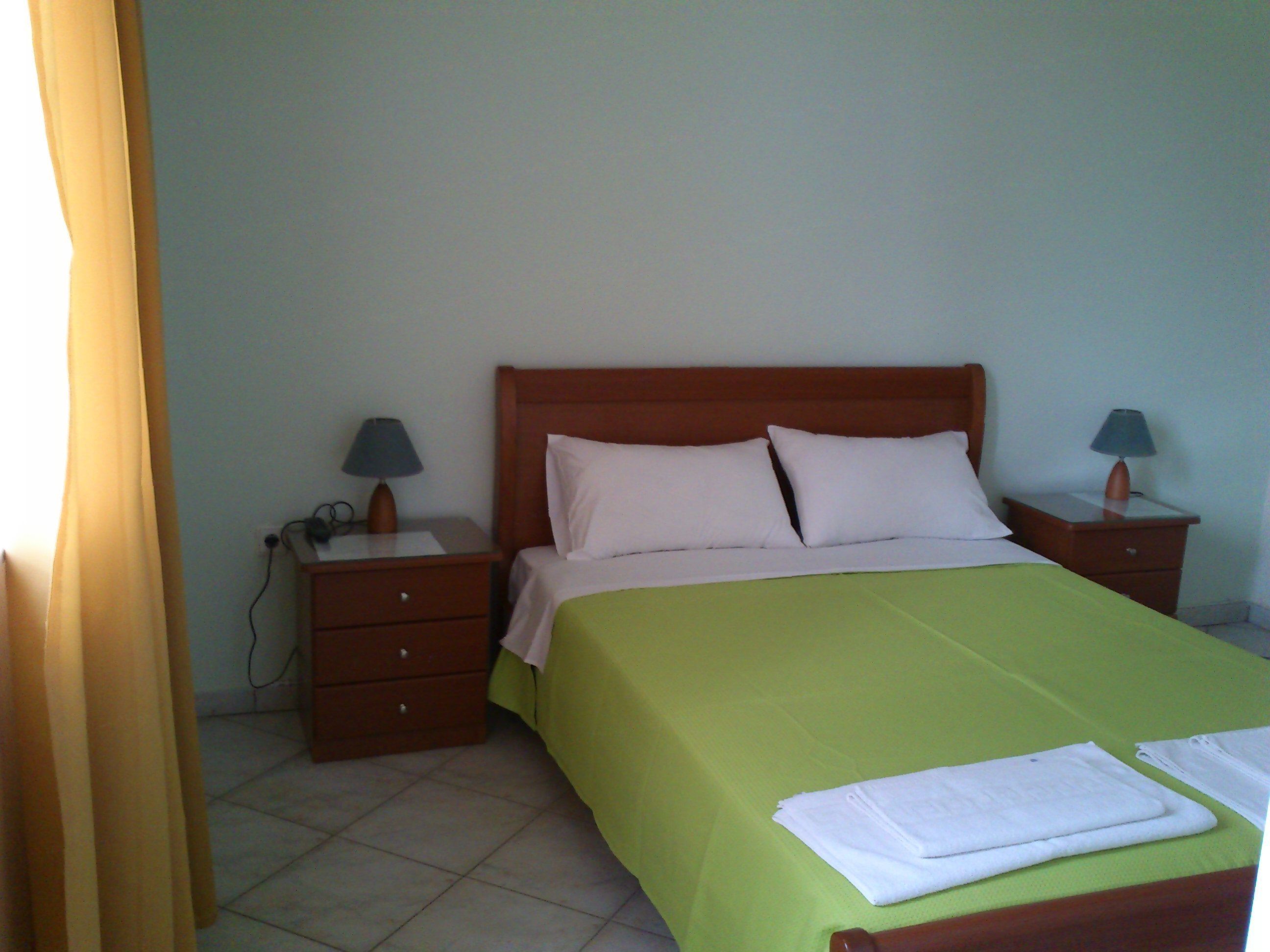 A neatly made bed with a green bedspread, two white pillows, and two bedside lamps on wooden nightstands.