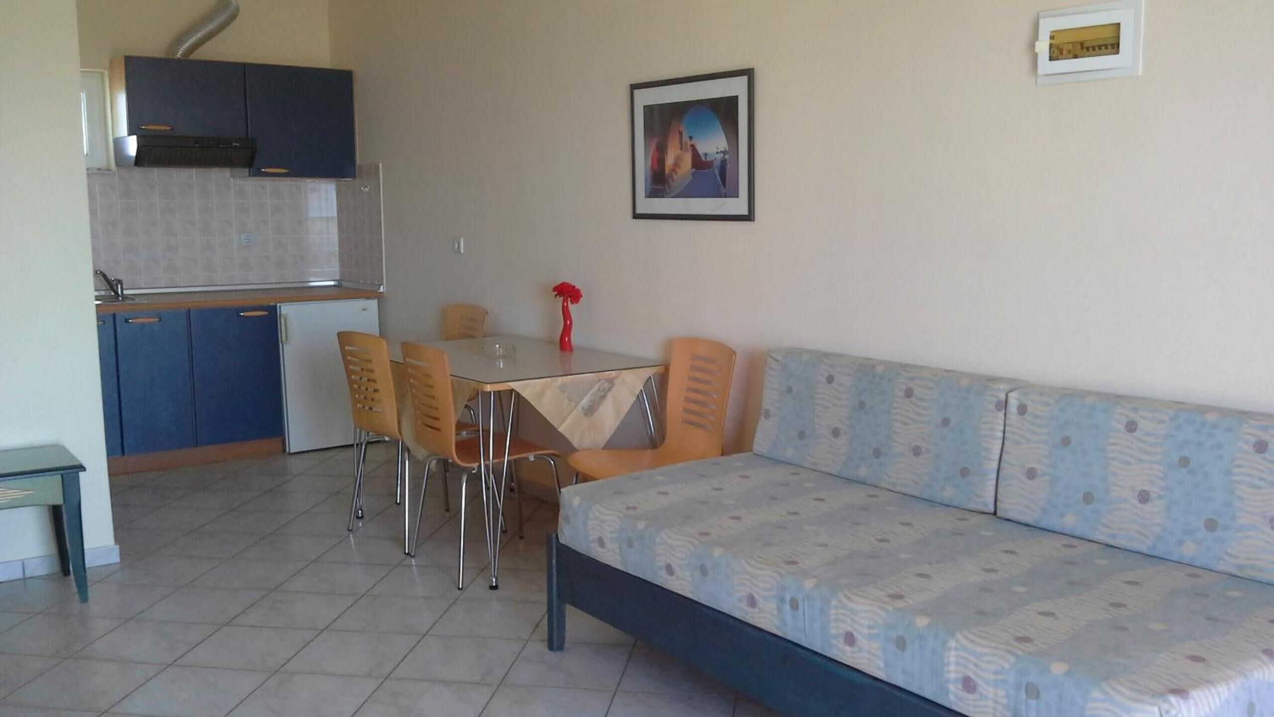 A compact living space with a kitchenette, a dining table with four chairs, a sofa, and a framed picture on the wall.