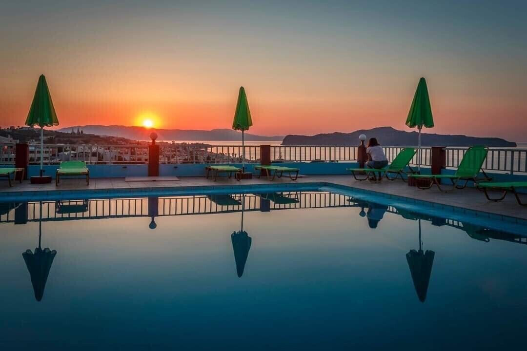 Una piscina en la azotea con sombrillas verdes, vista al atardecer y un paisaje urbano de fondo.