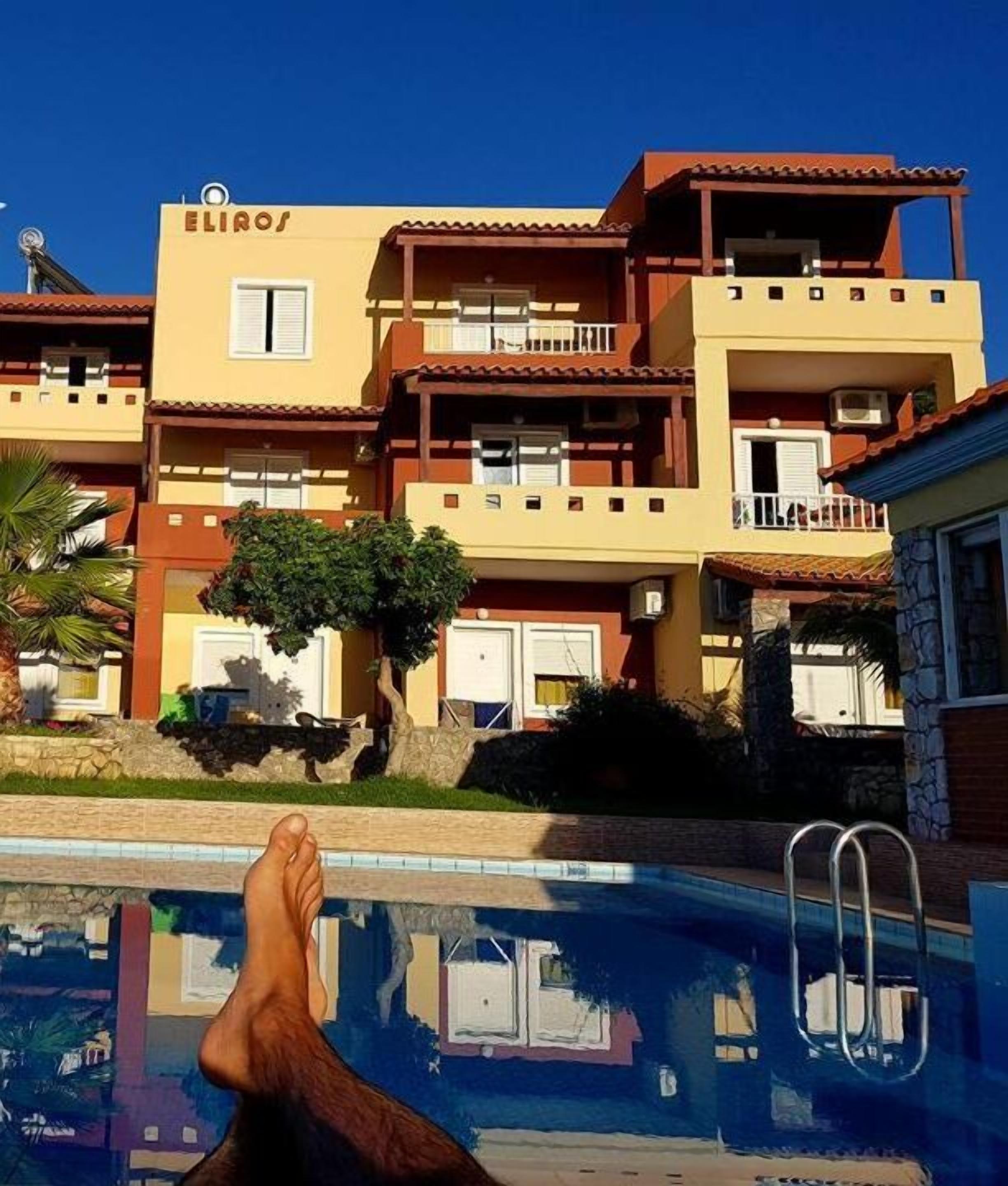 A hotel with a pool, a person relaxing by the pool, and a sign that reads "ELIROS".