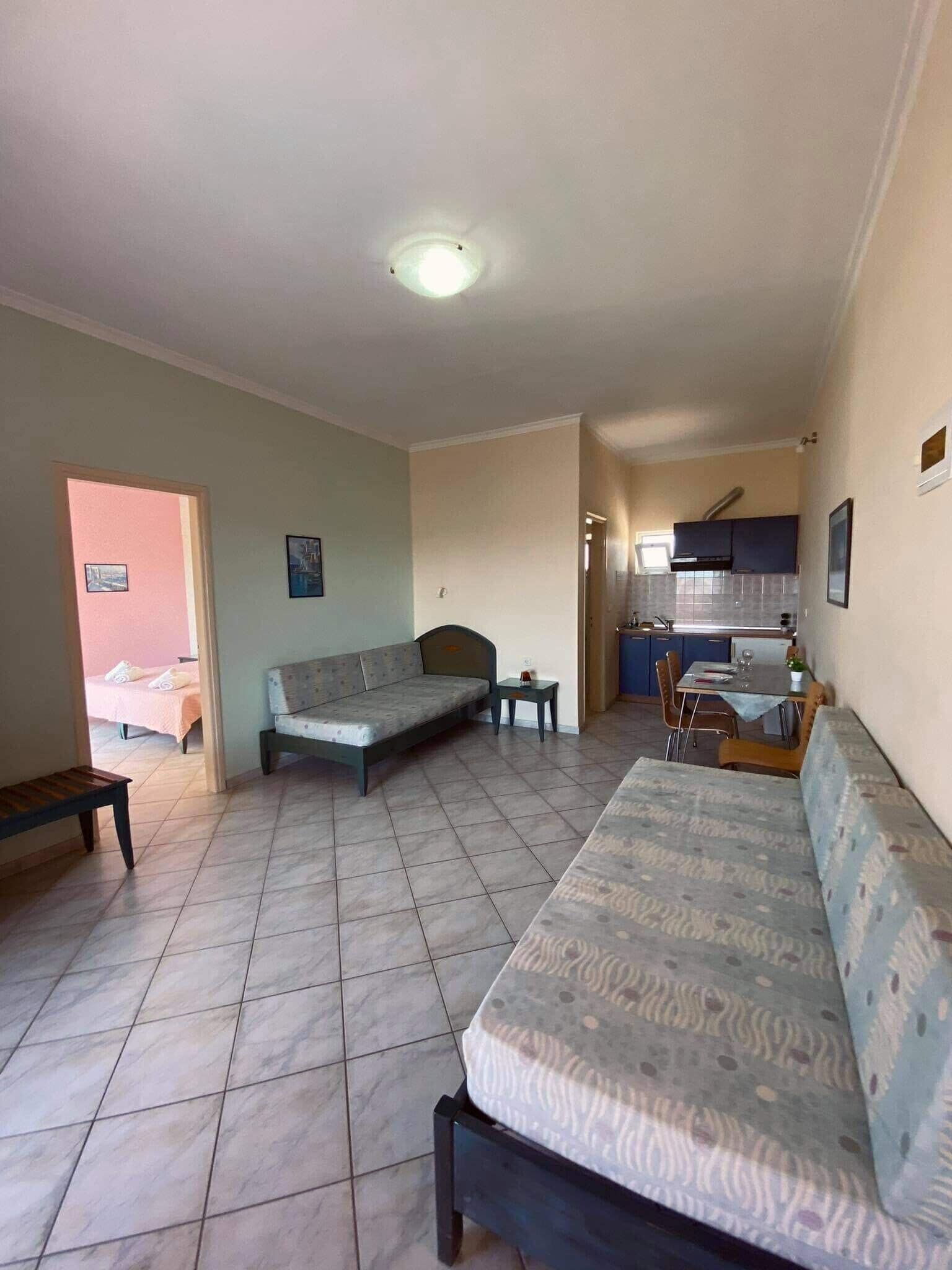 Ein geräumiges Zimmer mit einem großen Bett, einem Schlafsofa, einem kleinen Tisch und einer Küchenzeile im Hintergrund.