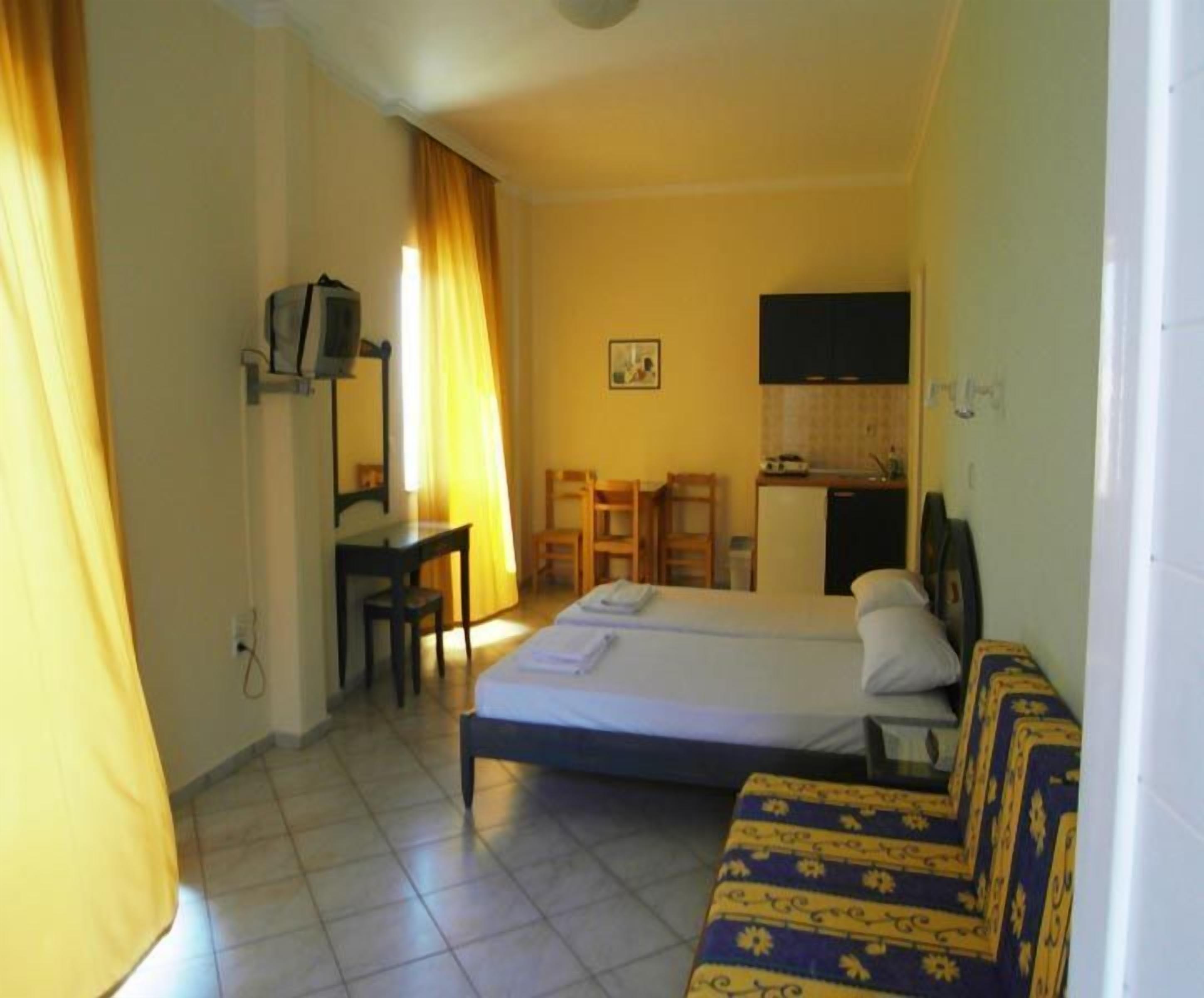 A hotel room with a bed, a sofa, a desk, a chair, a television, and a kitchenette.