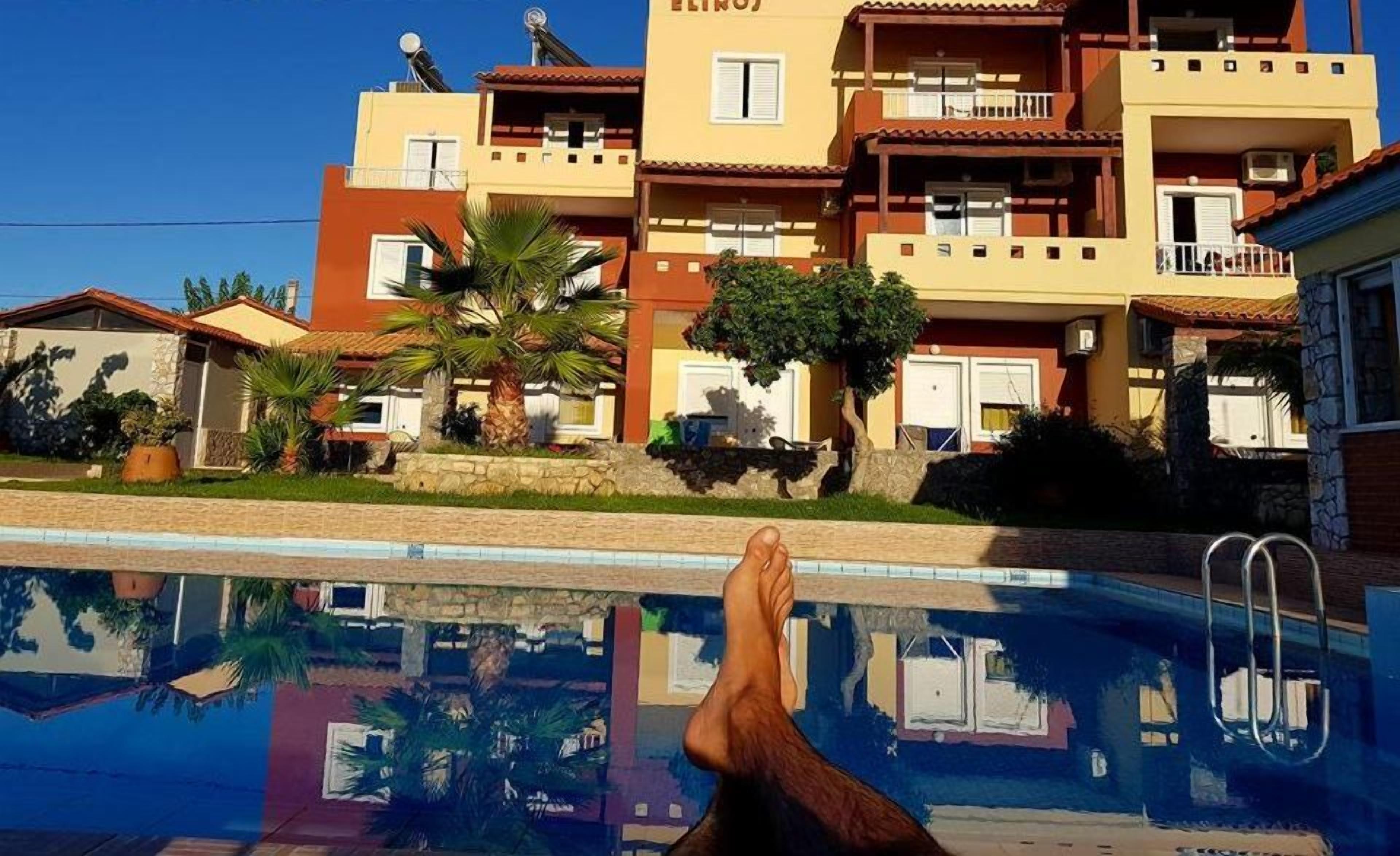 Un hotel chiamato ELIROS con piscina, palme e un cielo azzurro limpido.