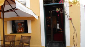 A yellow building with a wooden bench and chairs outside, a potted plant, and a statue on the window sill. - Solar das Artes Pousada Boutique (Salvador)