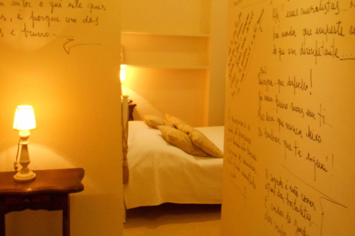 A room with a bed, a nightstand with a lamp, and walls covered with handwritten notes.