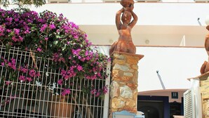 Un muro de piedra con carteles que indican opciones de comida y bebida, una escalera que conduce a un edificio con cúpulas azules y un árbol con flores púrpuras.