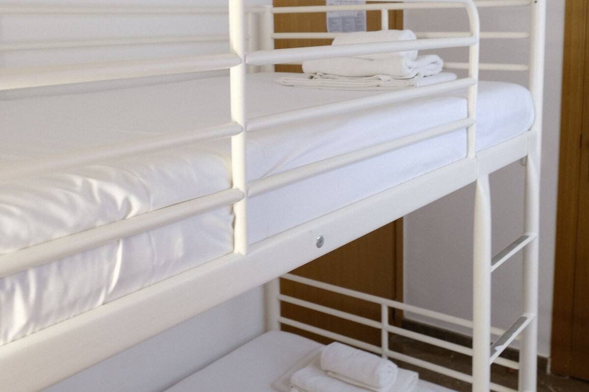 Un llit superposat amb roba de llit blanca i una porta de fusta al fons.