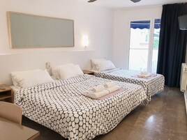 Habitación de hotel con dos camas, un ventanal con cortinas, un ventilador de techo y una lámpara fijada a la pared.