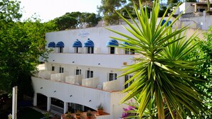 Un hotel de varios pisos con fachada blanca, toldos azules y una palmera en primer plano.
