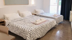 Habitación de hotel con dos camas, un ventanal grande, un ventilador de techo y una televisión montada en la pared.