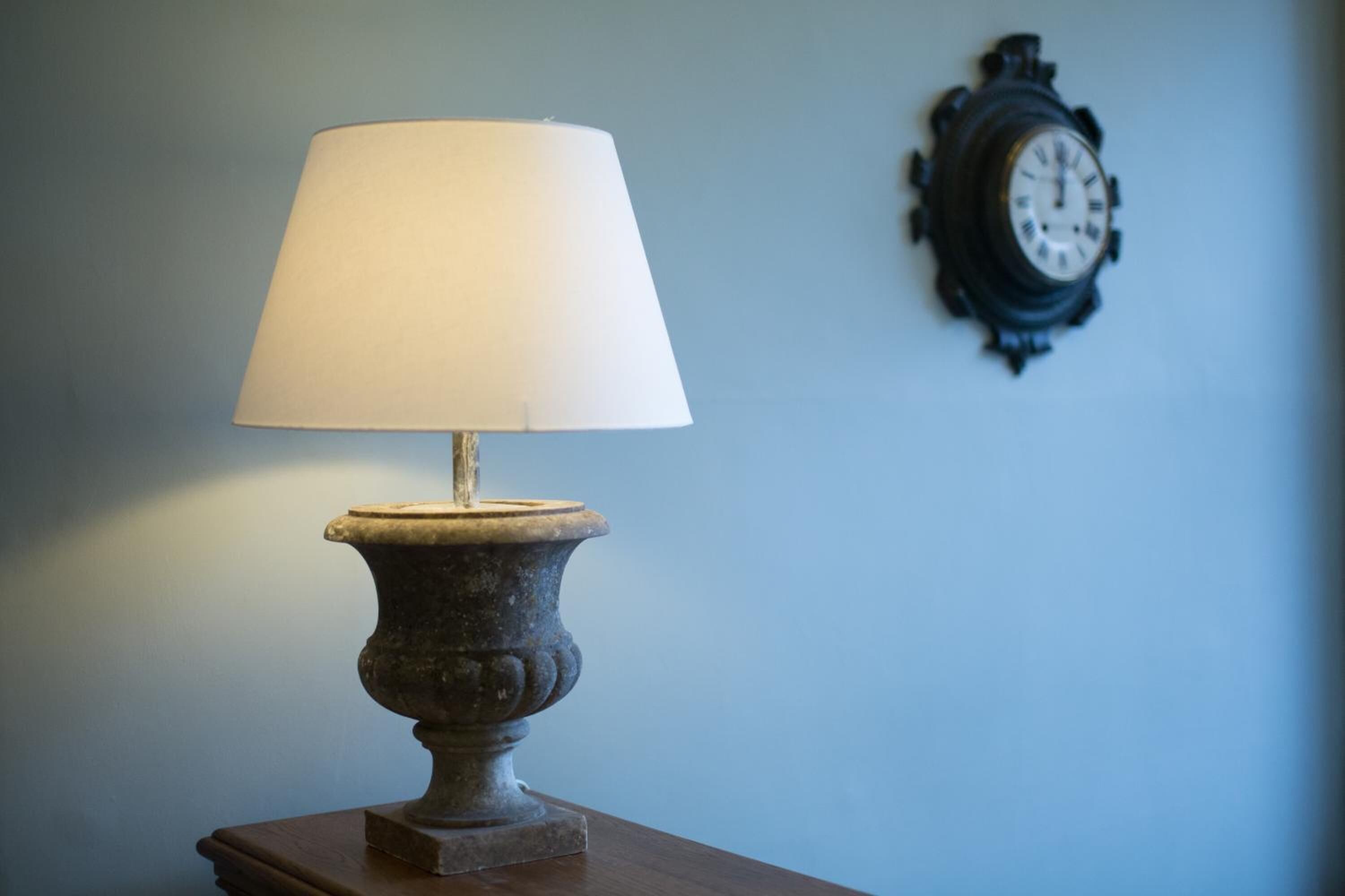 A table lamp with a white shade on a wooden table against a blue wall.