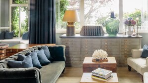 A living room with a dark sofa, a coffee table with books, a lamp, and a decorative vase. - Merchants Manor (Falmouth)