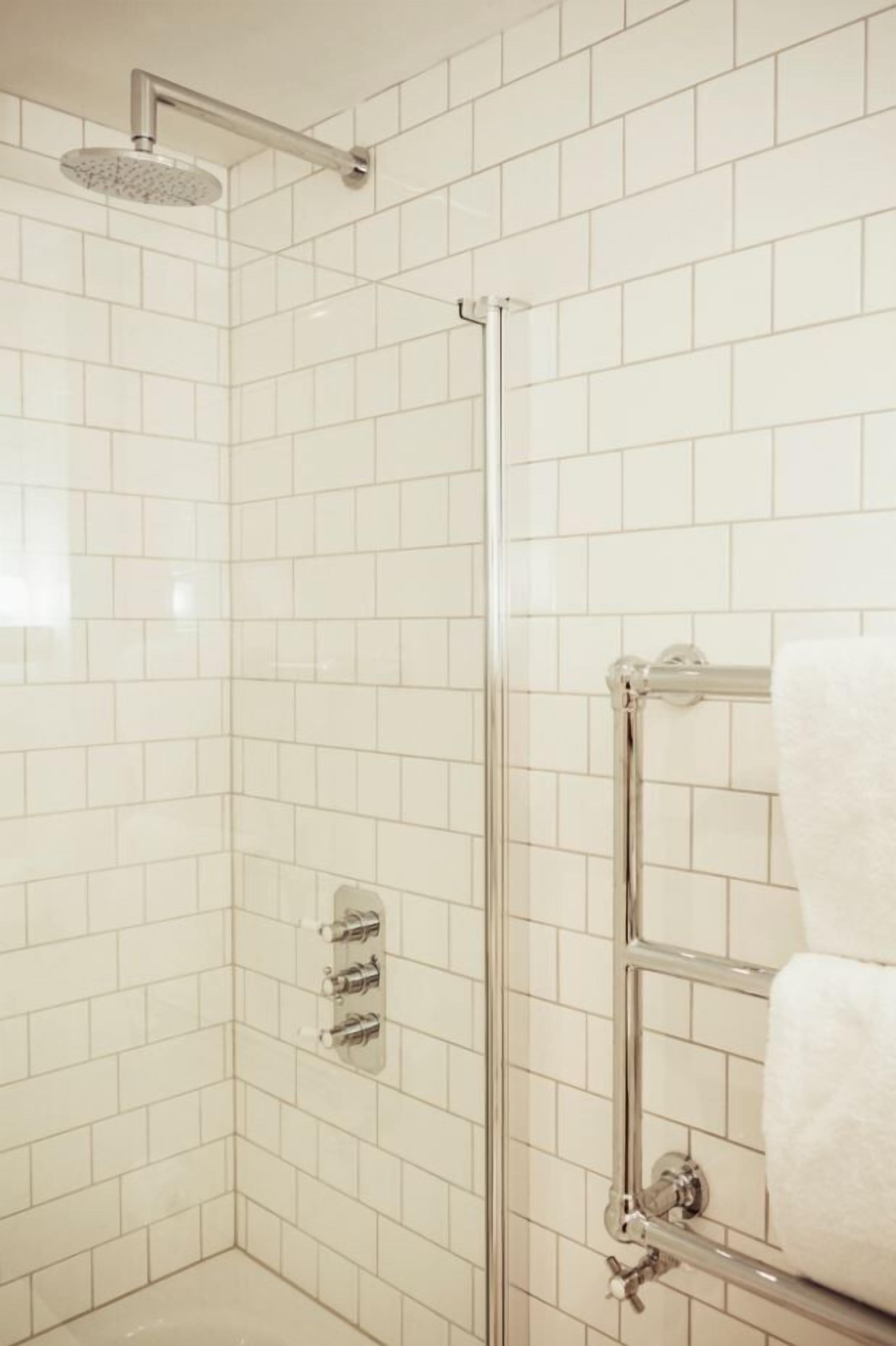 A corner shower with a glass door, chrome fixtures, and white tiled walls.