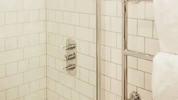 A corner shower with a glass door, chrome fixtures, and white tiled walls.
