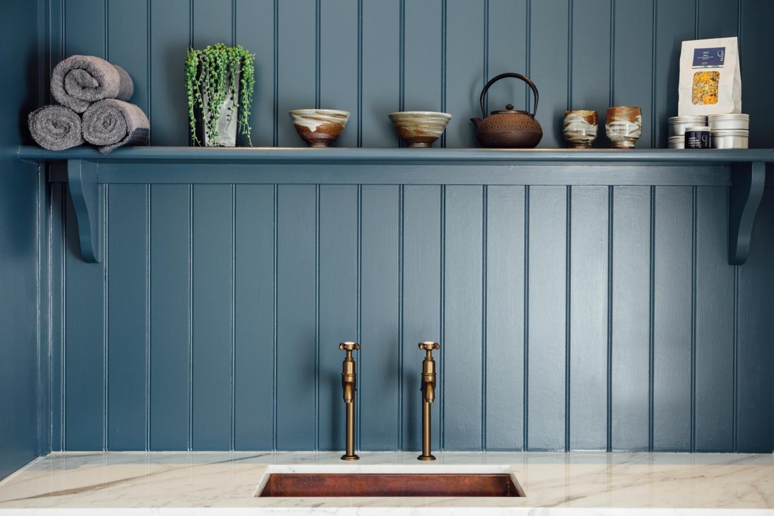 A bathroom with a blue wall, a marble sink, and various toiletries on a shelf.