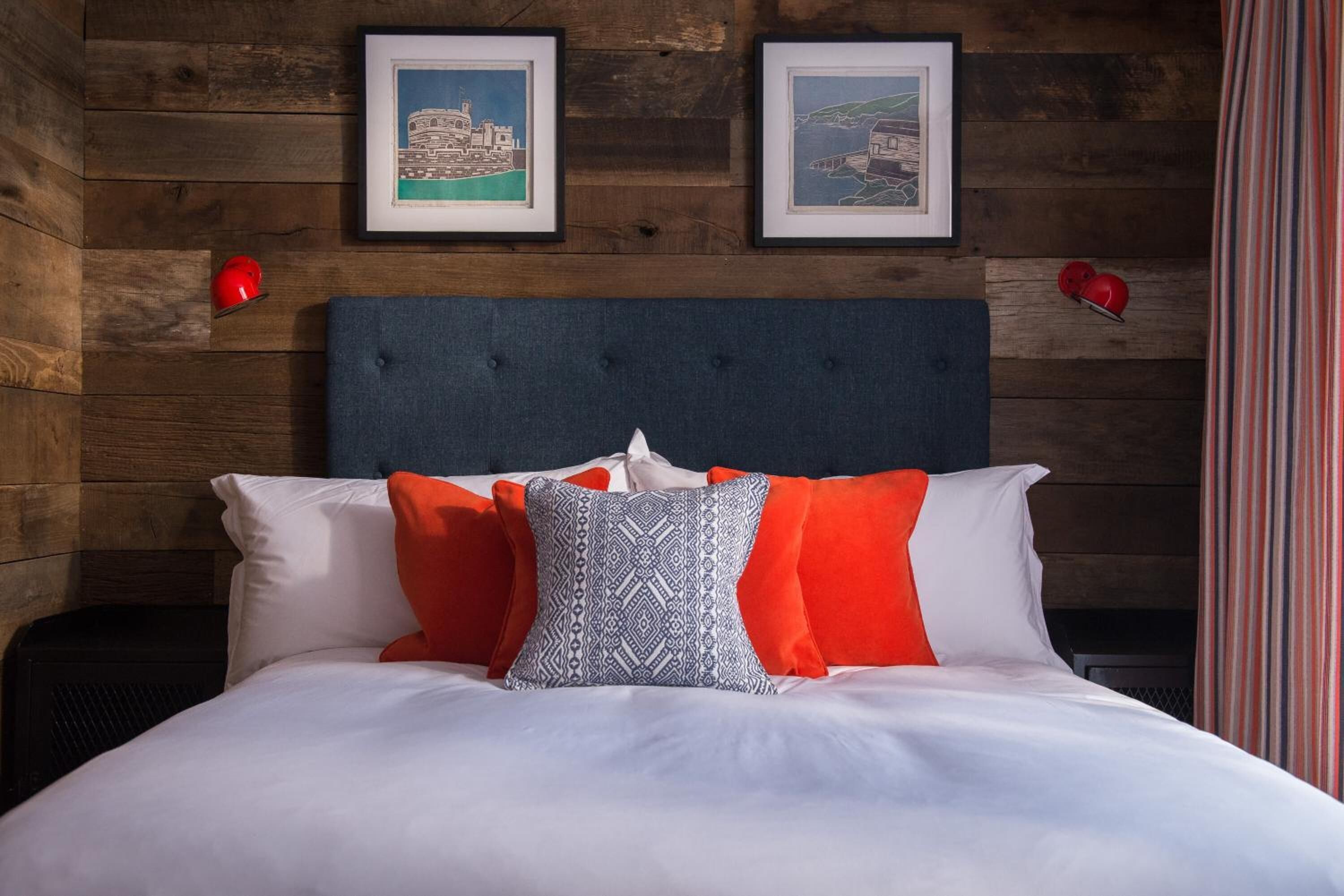 Una cama con ropa de cama blanca y naranja, un cabecero azul y dos cuadros en la pared.
