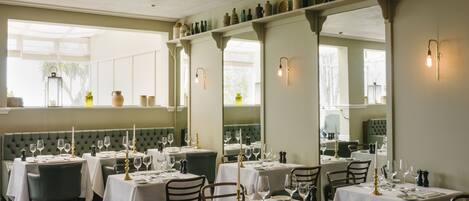 A restaurant with multiple tables set for dining, each with white tablecloths, candles, and wine glasses.