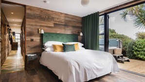 A bedroom with a wooden headboard, a large bed with white bedding, a nightstand, and a view of greenery outside. - Merchants Manor (Falmouth)