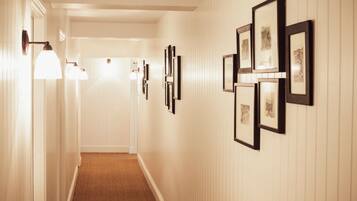 A hallway with framed pictures on the walls and wall-mounted lights.