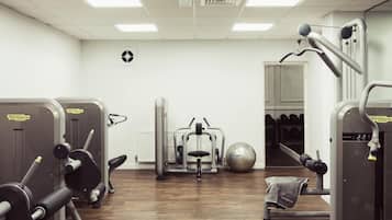 A gym with various exercise machines, a mirrored wall, and a door leading to a changing room.