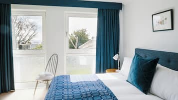 A bedroom with a bed, a chair, a bedside table, and a window with curtains.