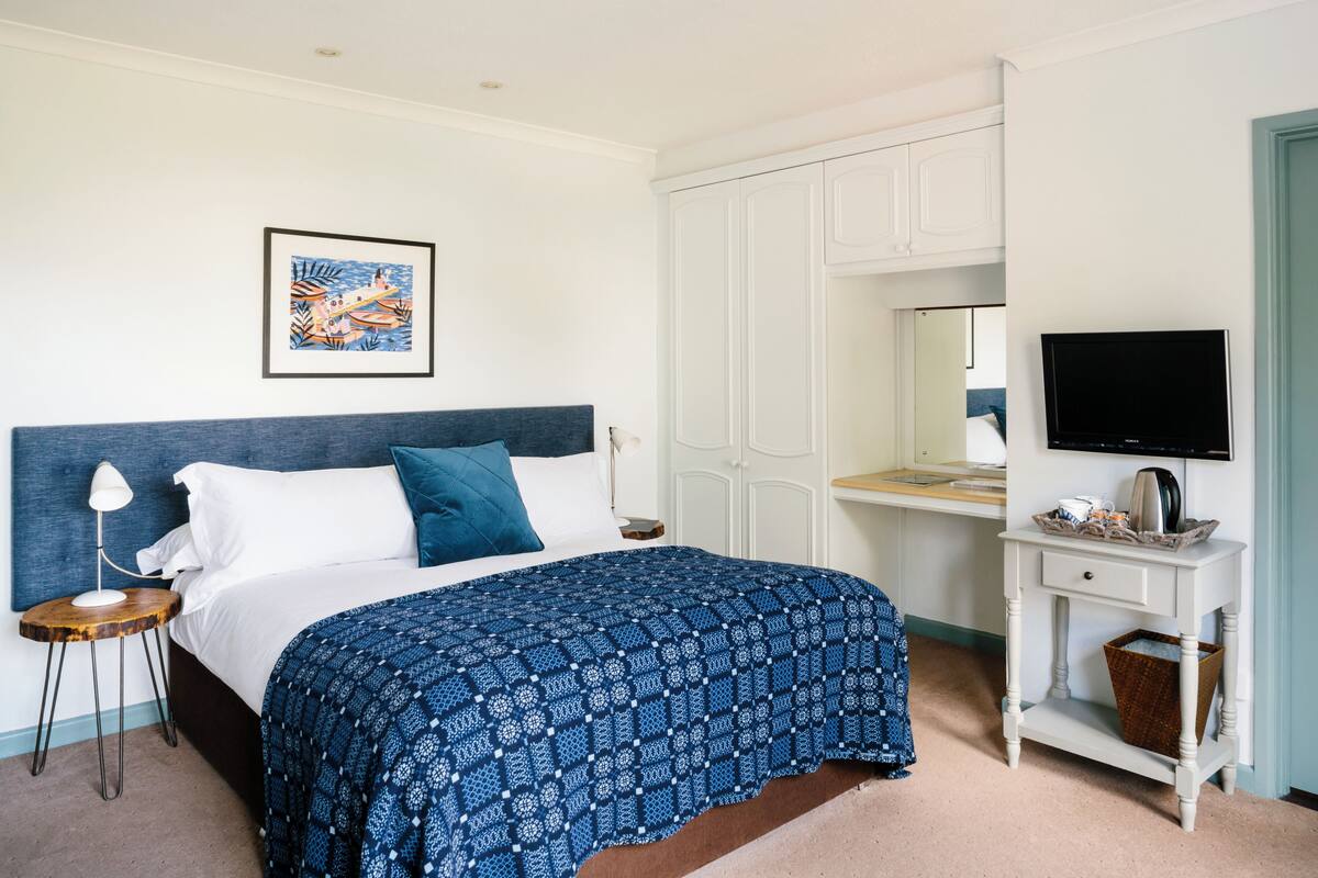 Une chambre à coucher bien rangée, avec un lit, une table de chevet, une lampe et un téléviseur posé sur un meuble.