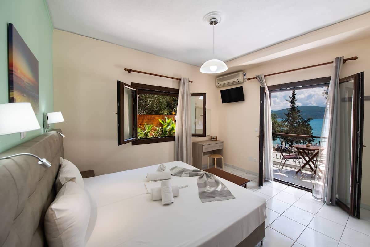Quarto de hotel com cama, escrivaninha, cadeira, televisão e varanda vista para o mar.