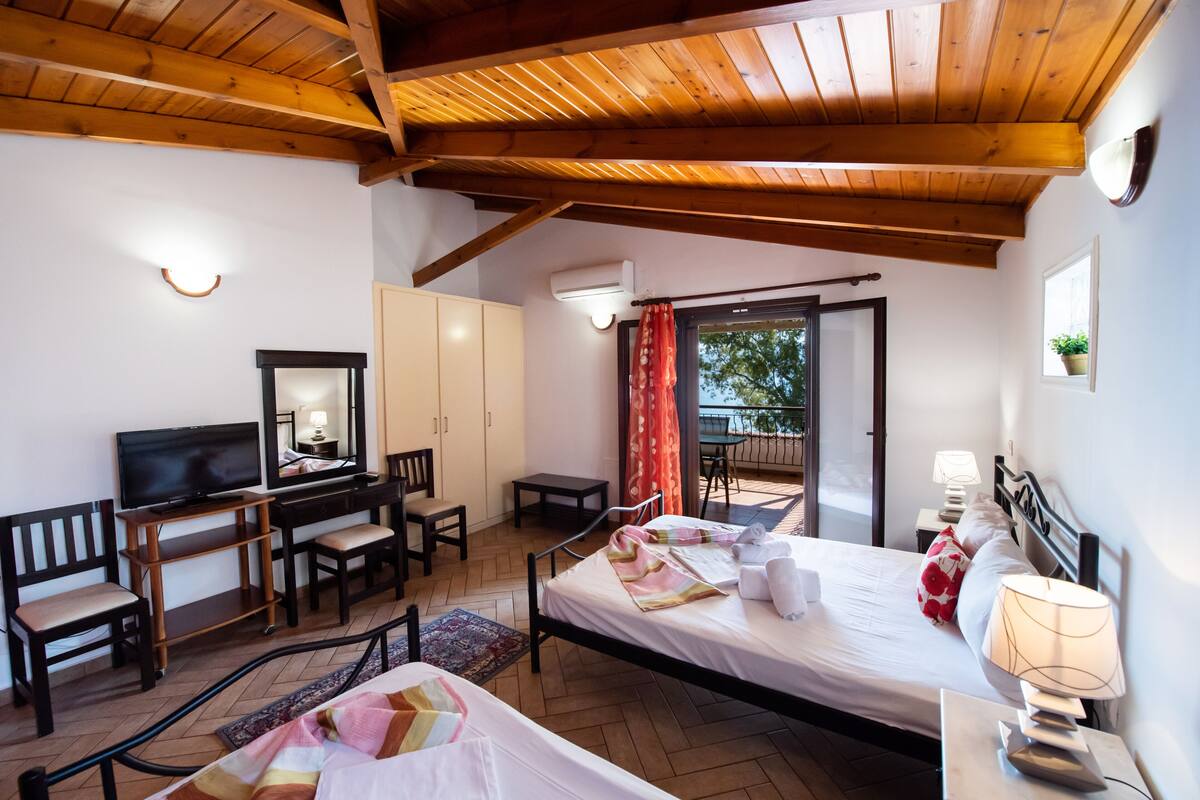 Um quarto com cama, escrivaninha, televisão e uma cadeira.