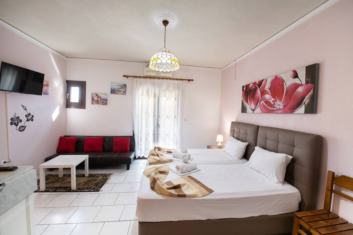 Quarto de hotel com duas camas, um sofá, uma televisão e um quadro na parede.
